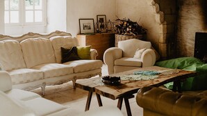 Un salon rustique avec des poutres apparentes, un canapé blanc, un fauteuil vert et une cheminée.