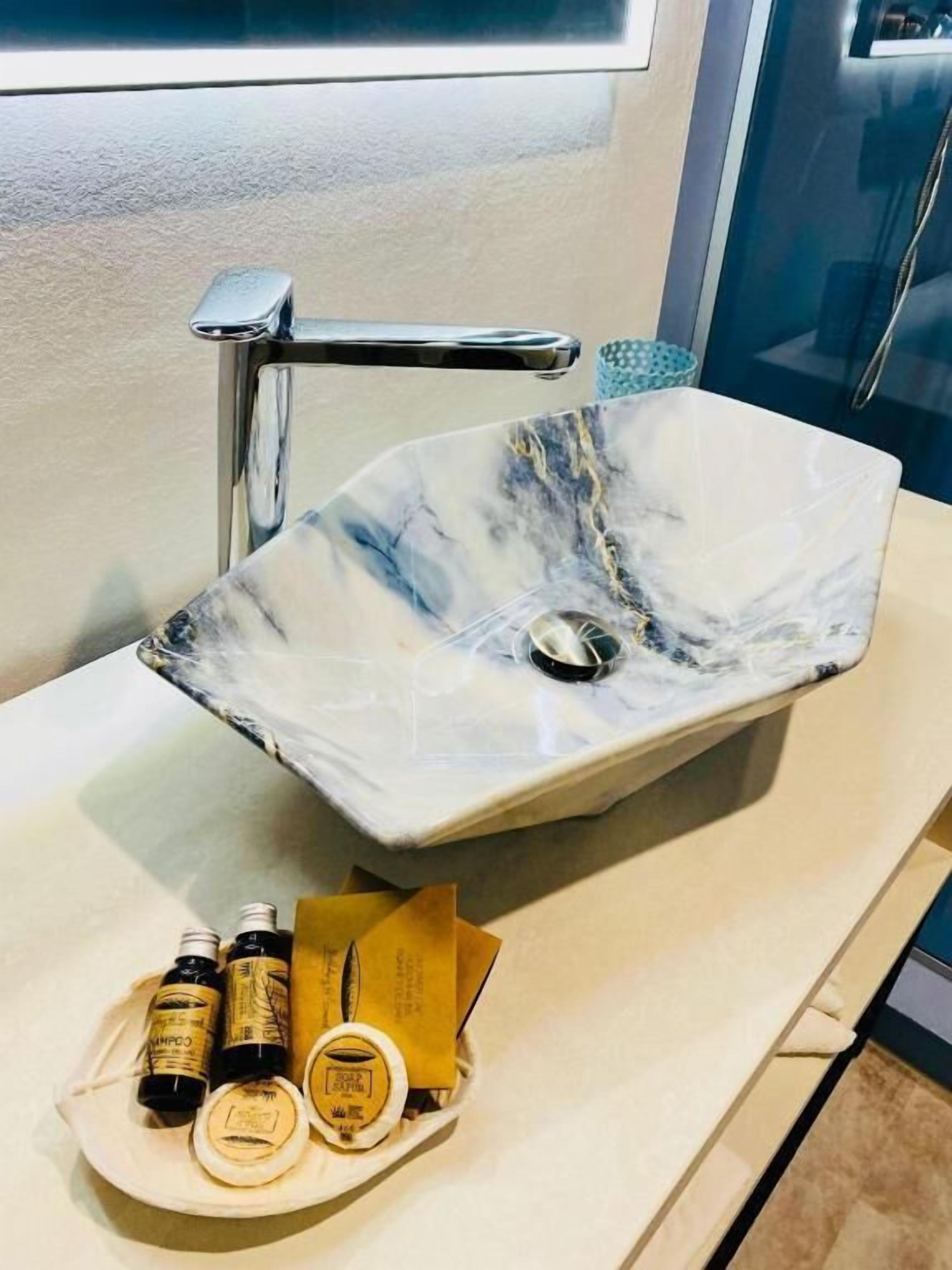 Un baño con lavamanos de mármol, grifo cromado y artículos de aseo en una bandeja.
