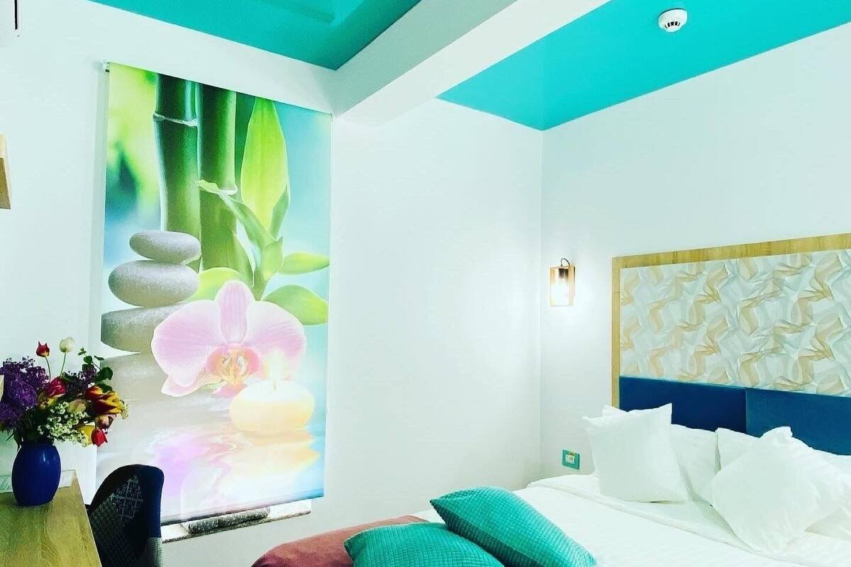 Ein Hotelzimmer mit Bett, Kissen, einer Vase mit Blumen und einer Wand mit einem Wandgemälde zum Thema Natur.