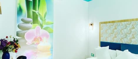 A hotel room with a bed, pillows, a vase with flowers, and a wall with a nature-themed mural.