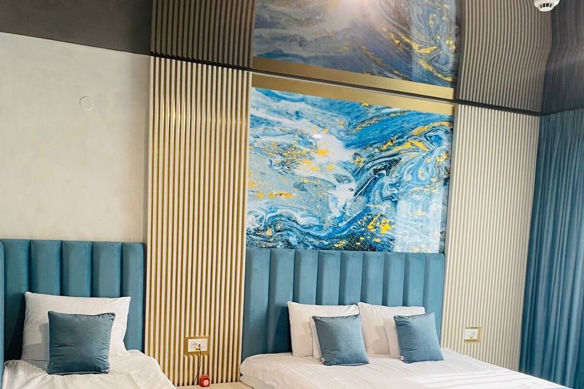 Ein modernes Hotelzimmer mit zwei Betten, einem großen abstrakten Gemälde und einer Deckenleuchte.