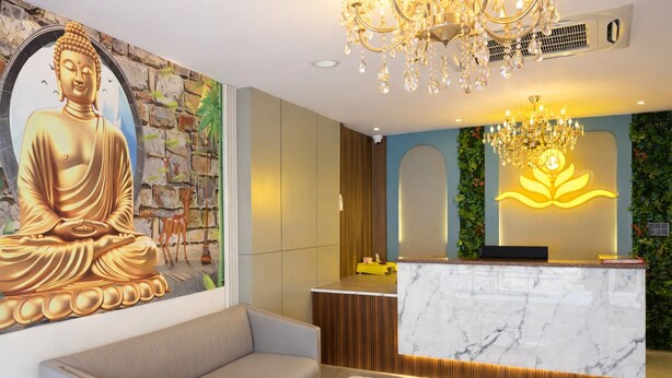 A reception area with a Buddha statue, a marble reception desk, a sofa, and a chandelier. - The Prominence Premium Hotel & Banquet  (Greater Noida)