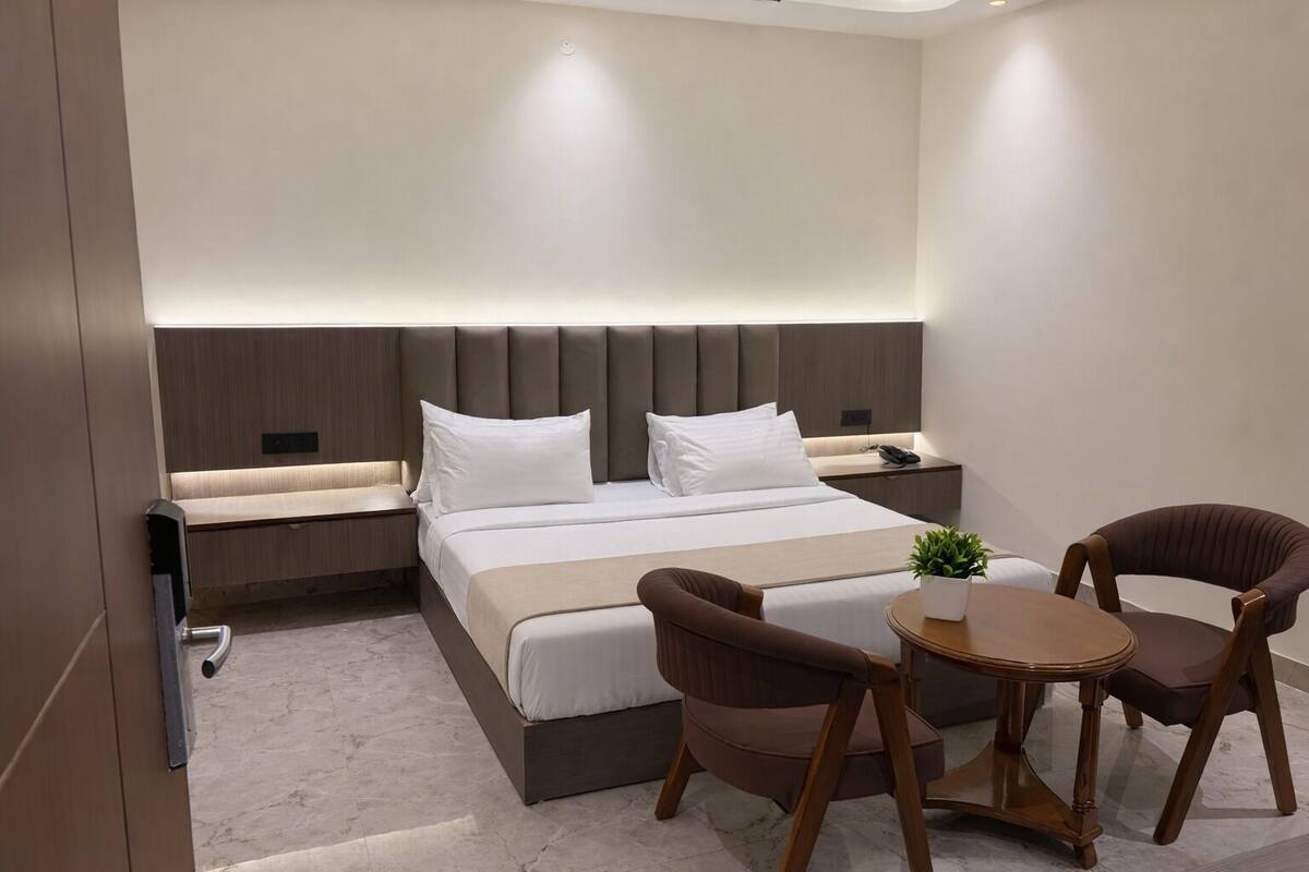 Una habitación de hotel moderna con una cama grande, mesitas de noche, una pequeña mesa redonda con sillas y una planta en maceta.