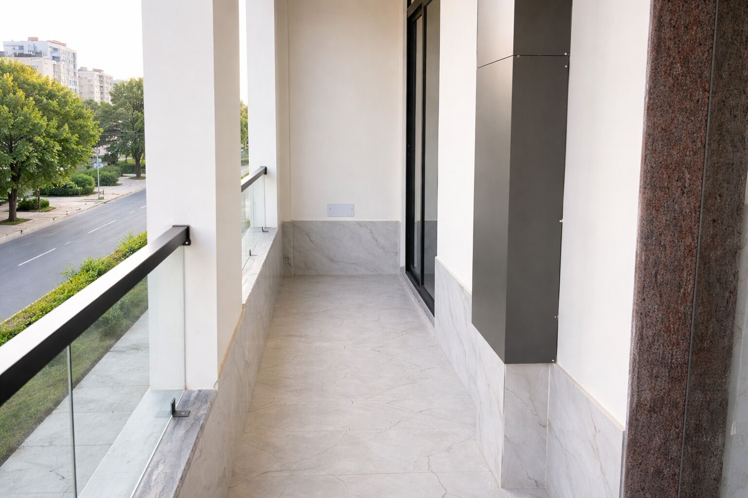 A balcony with a marble floor, a glass door, and a view of a street and buildings.