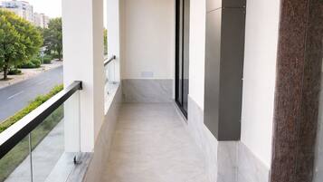A balcony with a marble floor, a glass door, and a view of a street and buildings.