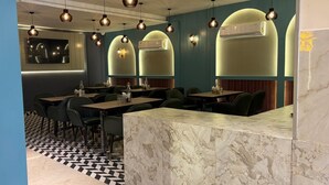 A restaurant interior with marble counters, black and white checkered flooring, and pendant lighting. - The Prominence Premium Hotel & Banquet  (Greater Noida)