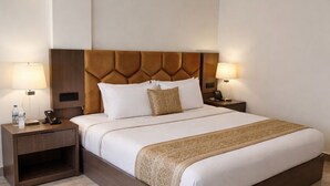 A hotel room with a large bed, two bedside tables, a headboard, and a nightstand. - The Prominence Premium Hotel & Banquet  (Greater Noida)