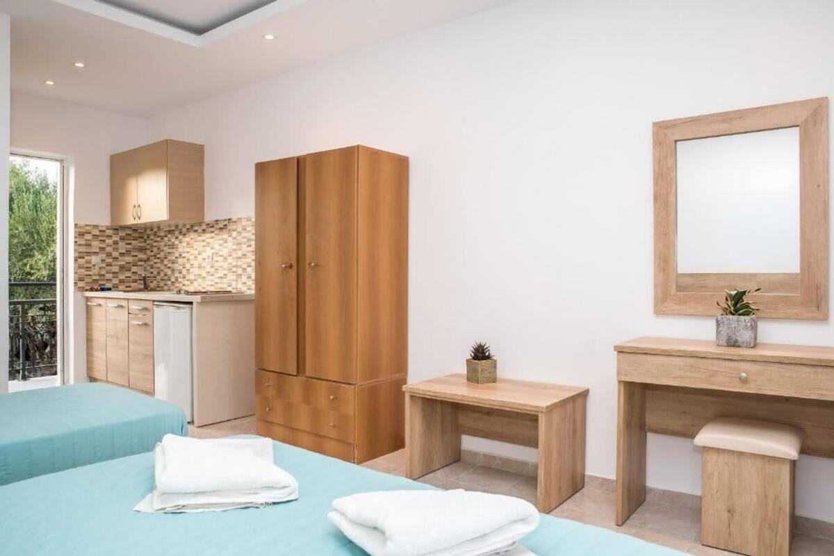 A modern bedroom with two beds, a wooden wardrobe, a small bedside table, a mirror, and a view of the kitchen.