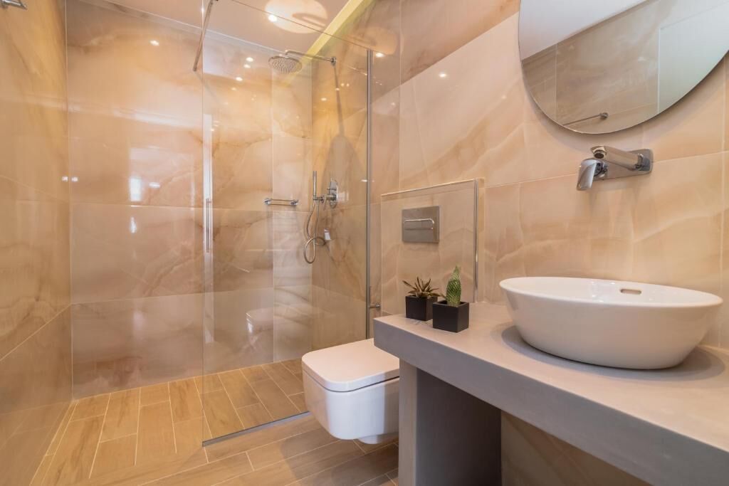 Un baño moderno con ducha de vidrio, lavamanos blanco y retrete.