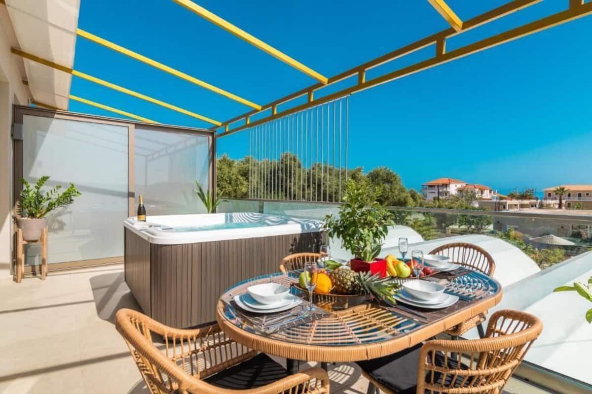 A balcony with a hot tub, dining table, chairs, and potted plants.