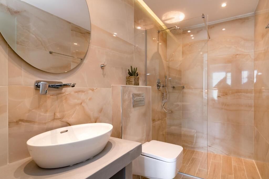 A modern bathroom with a large oval sink, a toilet, and a glass-enclosed shower.