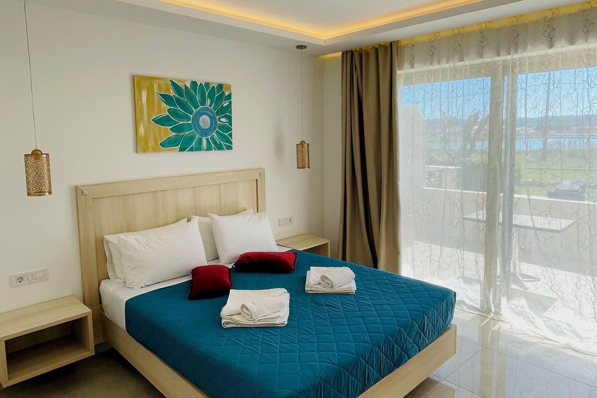 A modern hotel room with a large bed, a view of the outdoors, and a ceiling light fixture.