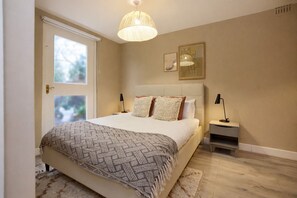 A bedroom with a bed, bedside tables, a hanging light fixture, and artwork on the wall. - West of Brick & Bloom (Kingston Upon Thames)