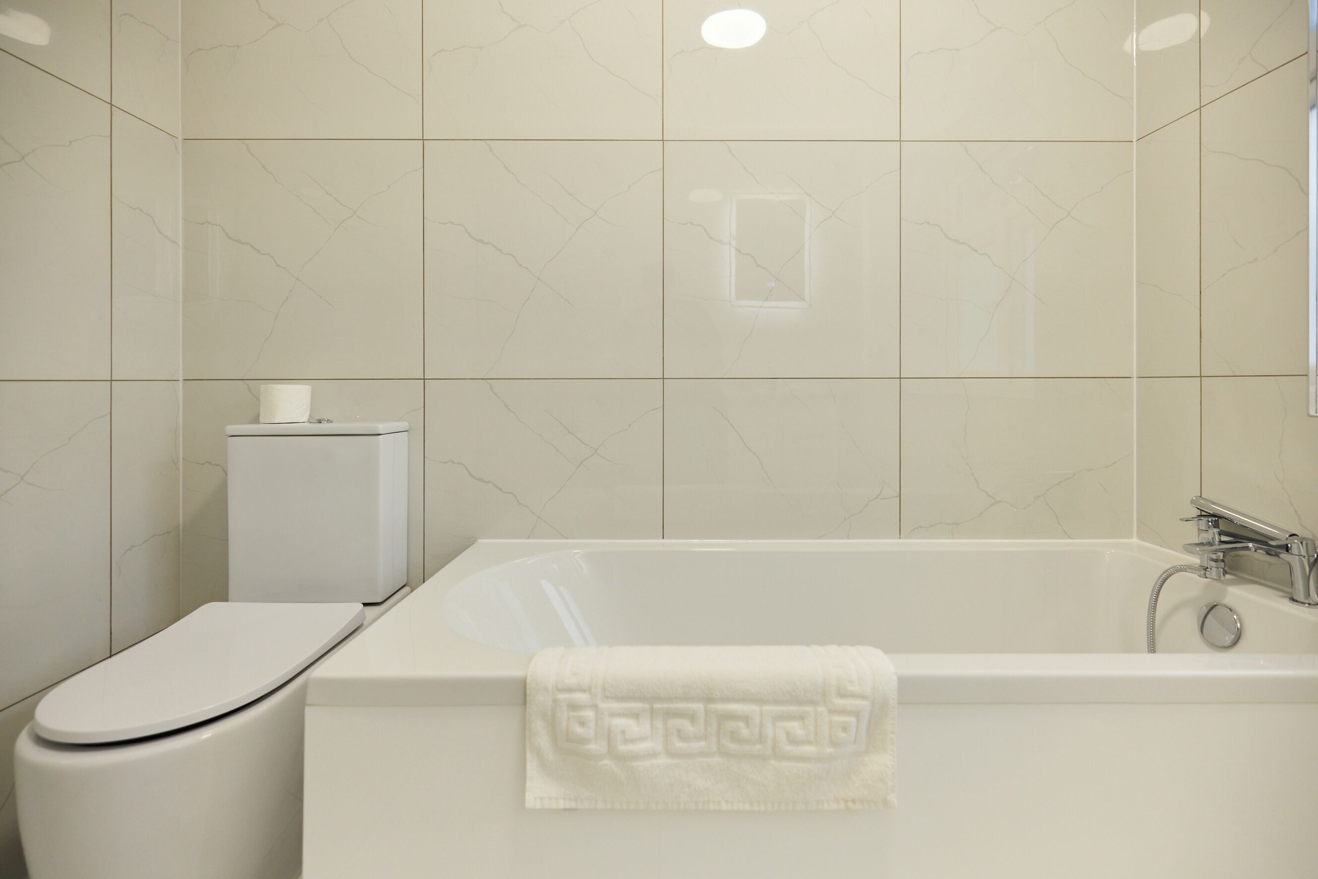 A modern bathroom with a toilet, a bathtub, and a towel.