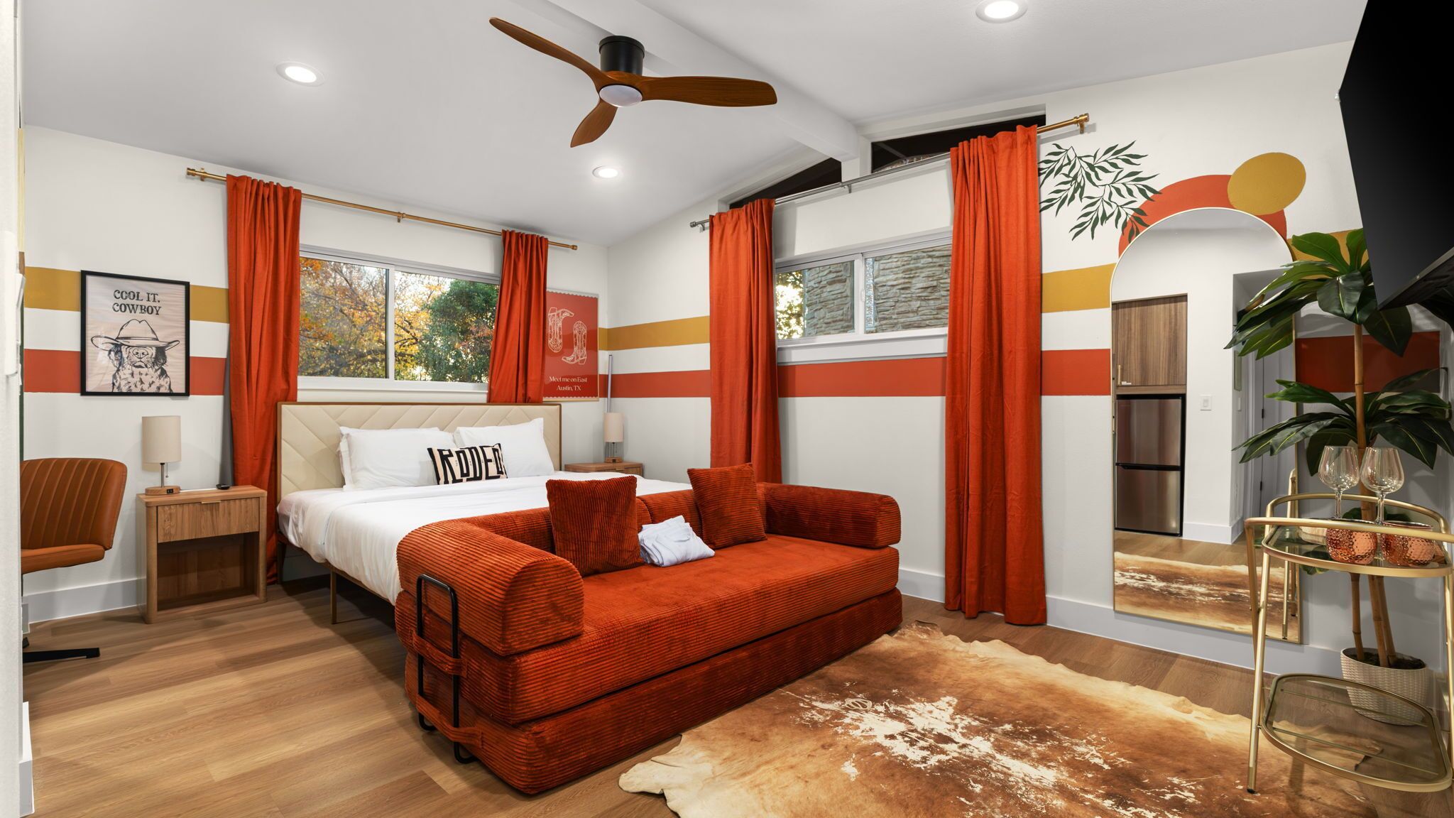 Een moderne slaapkamer met een bed, een rode bank, een houten vloer en een plafondventilator.