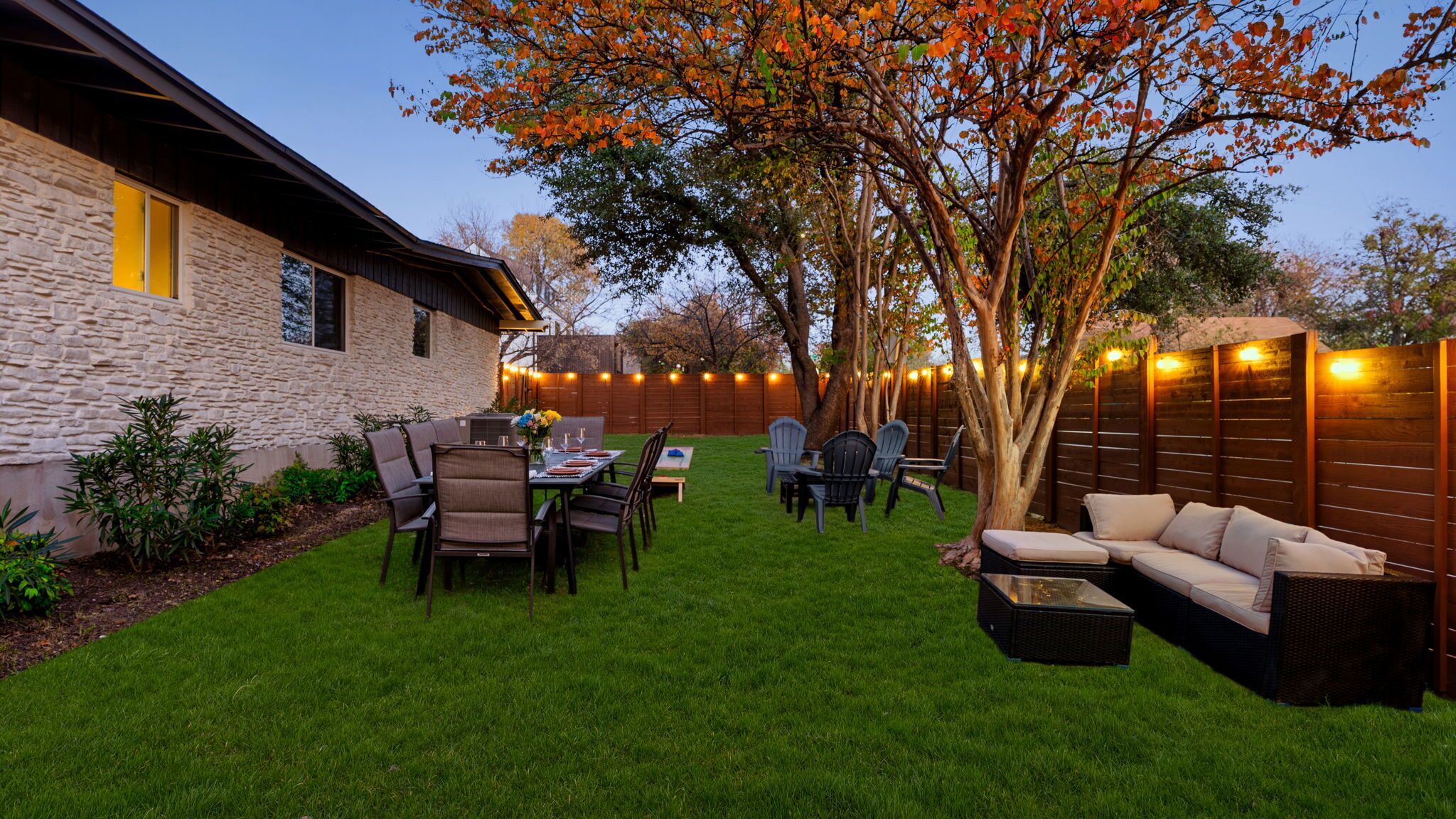 A backyard with a stone wall, outdoor furniture, and a tree.