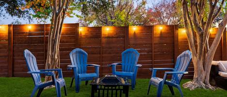 A backyard with a wooden fence, four blue chairs, a small table, and a tree.