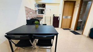 Een compacte keuken met een eethoek, inclusief een tafel, stoelen, een kleine plant en een koelkast.