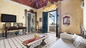 A room with a large bed, a television, a console table with framed pictures, a red and white patterned rug, and a view of the outside. - Residenza Crocione - Terrace sea view (Positano)
