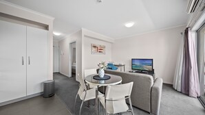 A modern hotel room with a dining area, a sofa, a TV, and a view of the outdoors. - Bright 1-bed Apartment in Greenway (Canberra)
