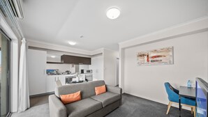 A modern living room with a grey sofa, a blue chair, and a flat-screen TV. - Bright 1-bed Apartment in Greenway (Canberra)