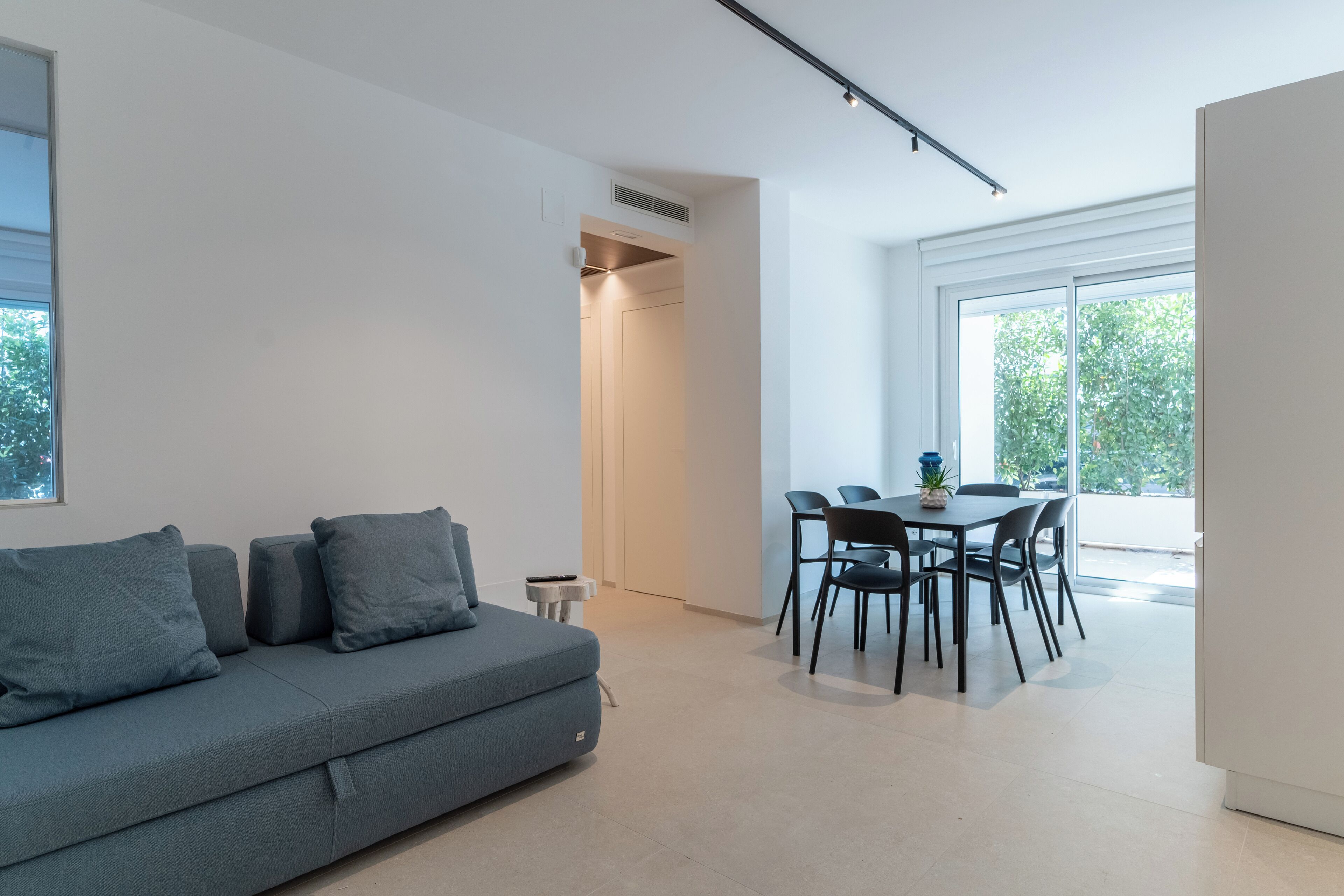 Ein modernes Wohnzimmer mit einer grauen Couch, einem Esstisch mit Stühlen und einem großen Fenster, das natürliches Licht hereinlässt.