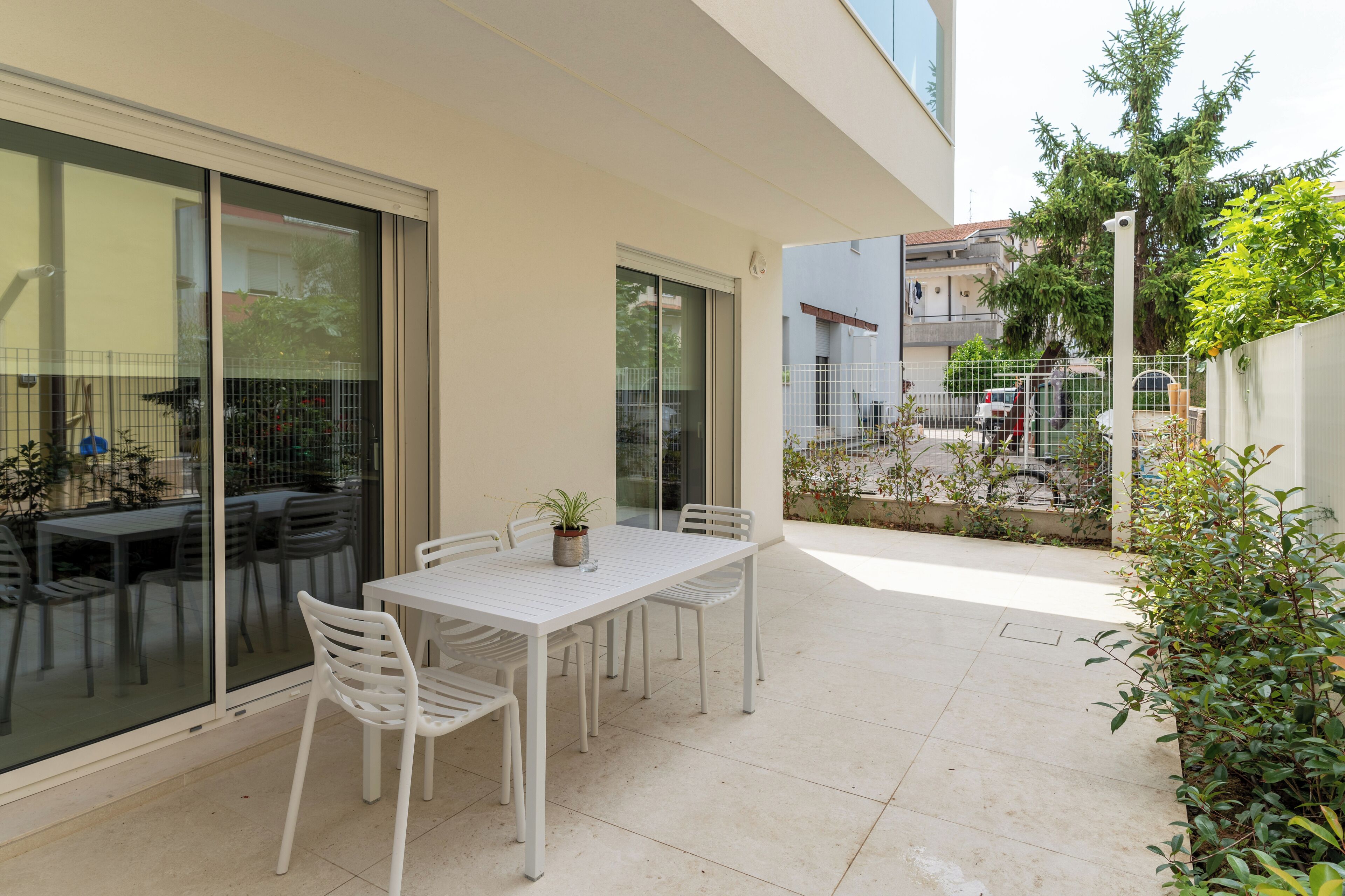 A patio with a white table and chairs, a potted plant, and a glass door leading to a balcony.