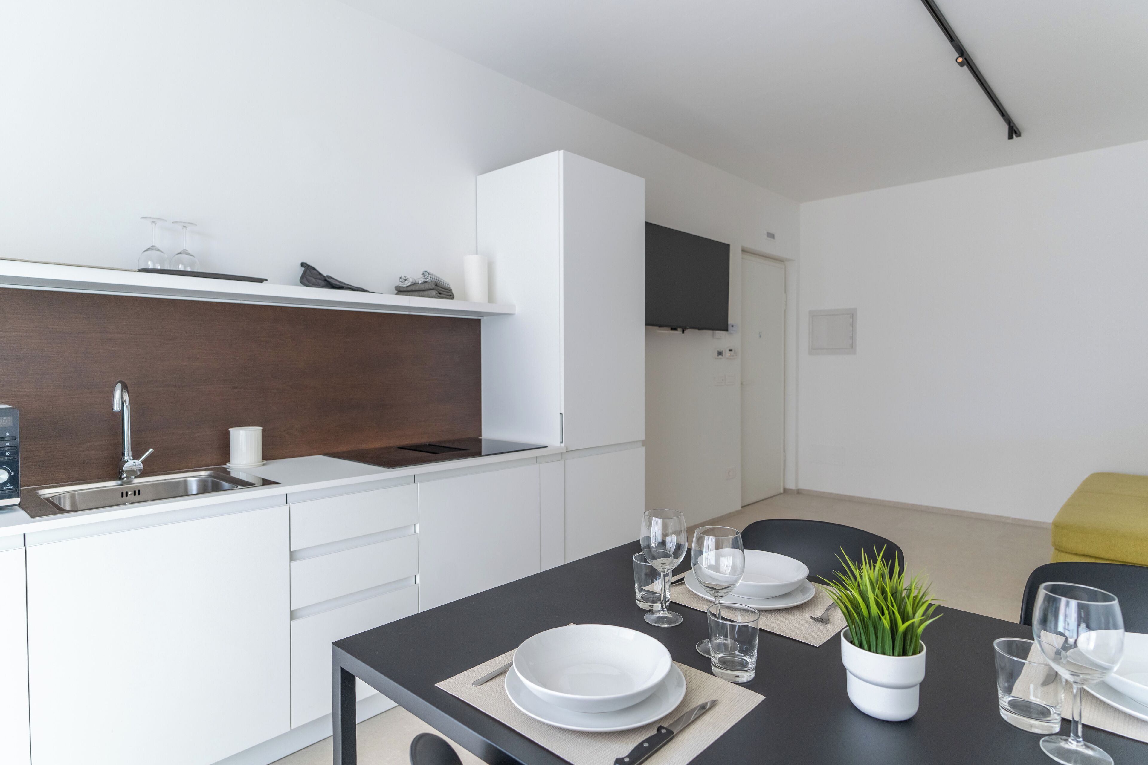 Et moderne køkken med hvide skabe, en sort bordplade og et spiseområde med et bord dækket til to.