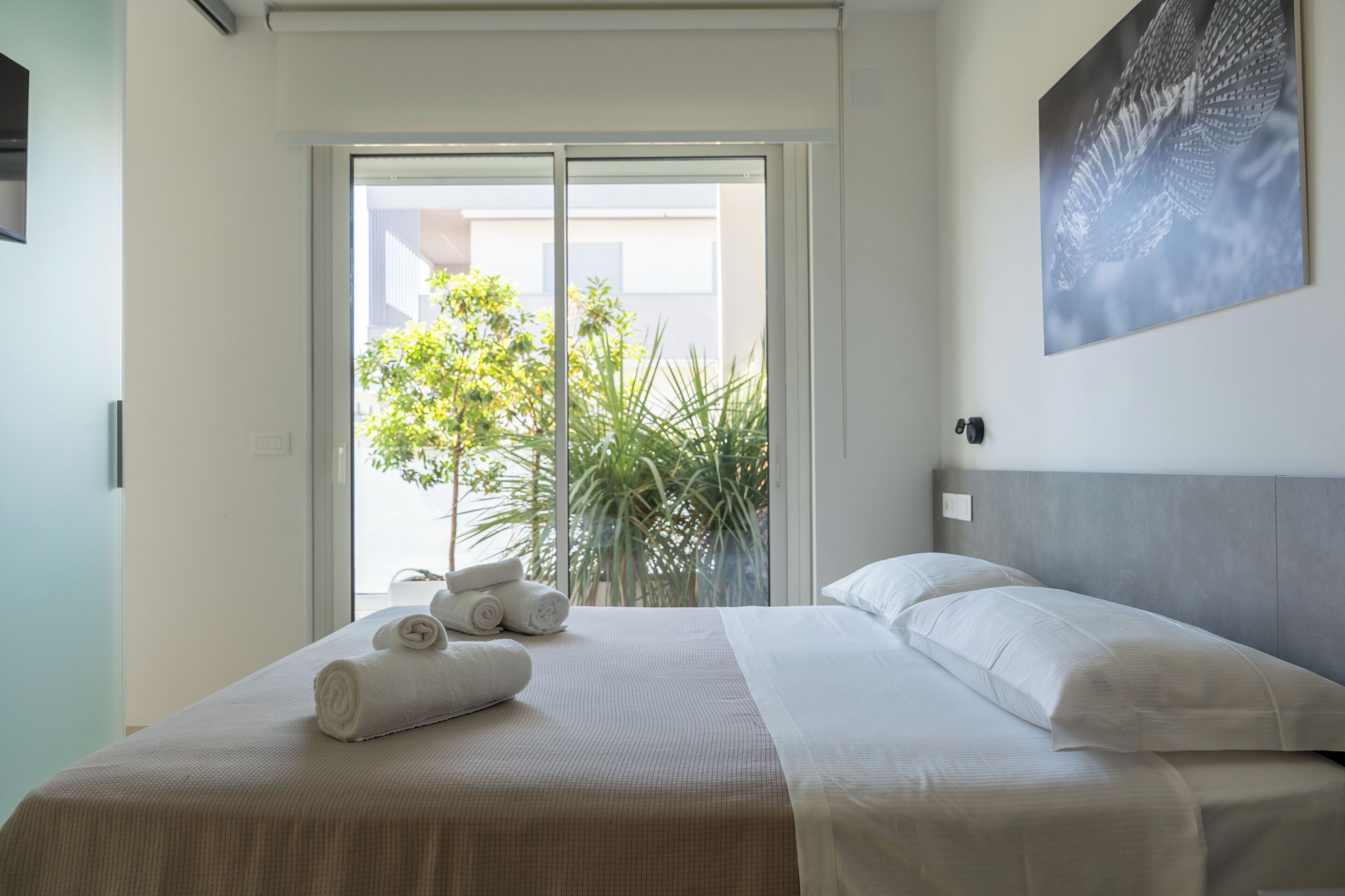 A hotel room with a bed, a large window, and a view of greenery outside.