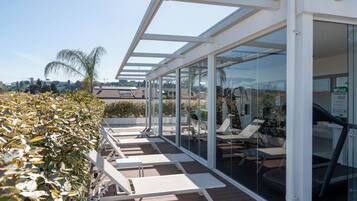 A covered outdoor area with glass walls, seating, and a view of the surrounding landscape.