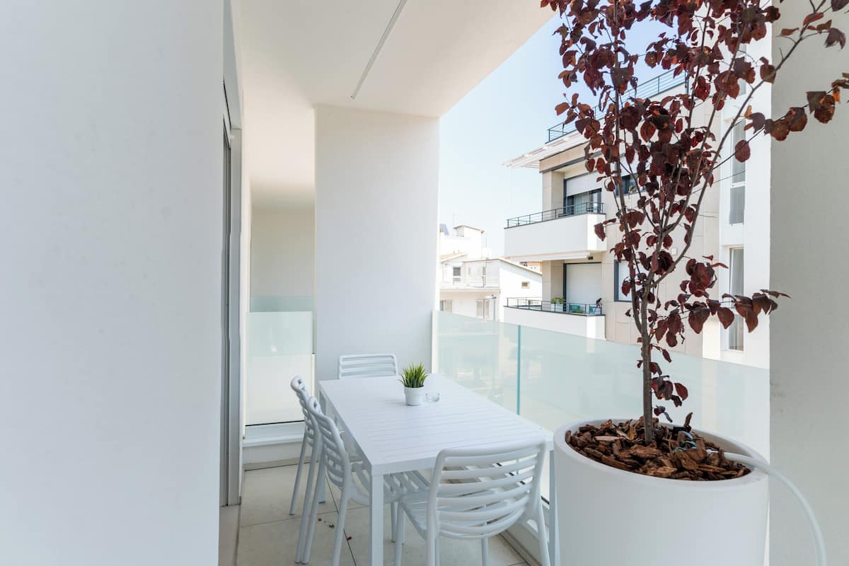 A balcony with a white table and chairs, a potted plant, and a view of adjacent buildings.