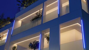 Un immeuble moderne à plusieurs étages, doté de balcons, de grandes fenêtres et d’éléments d’éclairage bleus qui mettent en valeur l’ensemble.