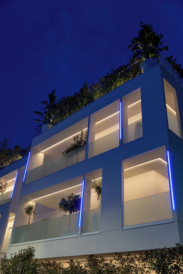 A modern multi-story building with balconies, large windows, and blue lighting accents.