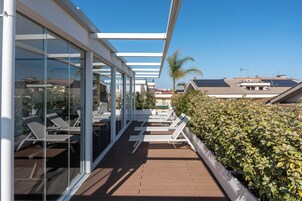 Un balcón con sillones de sol, una pared de vidrio y un seto.