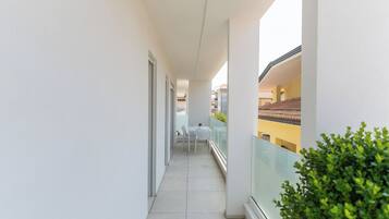 Een smalle gang met een glazen balustrade aan één kant, die leidt naar een balkon met uitzicht op een geel gebouw.