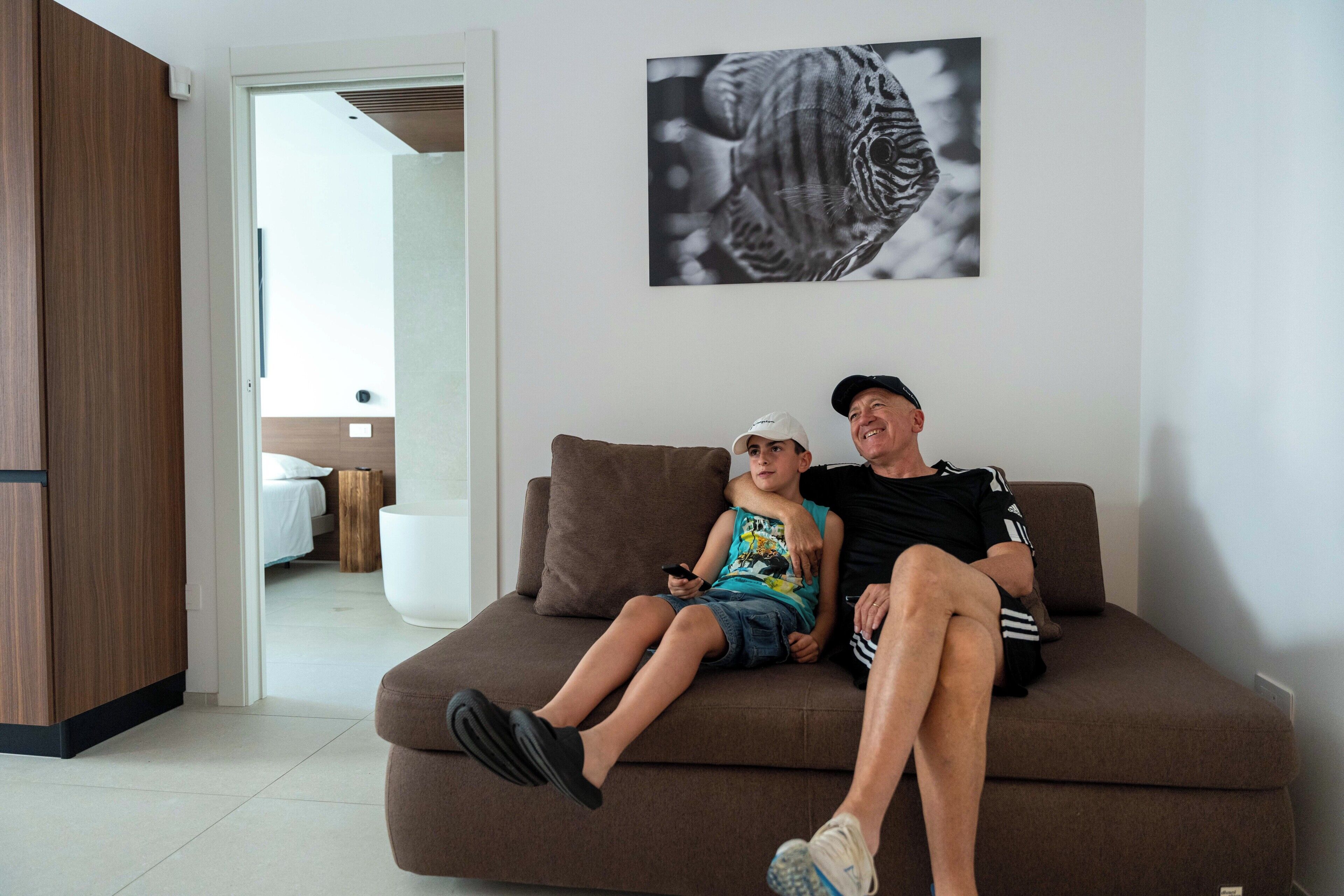 Ein modernes Wohnzimmer mit einem braunen Sofa, auf dem ein Kind und ein Erwachsener sitzen, und einem großen Schwarz-Weiß-Kunstwerk an der Wand.