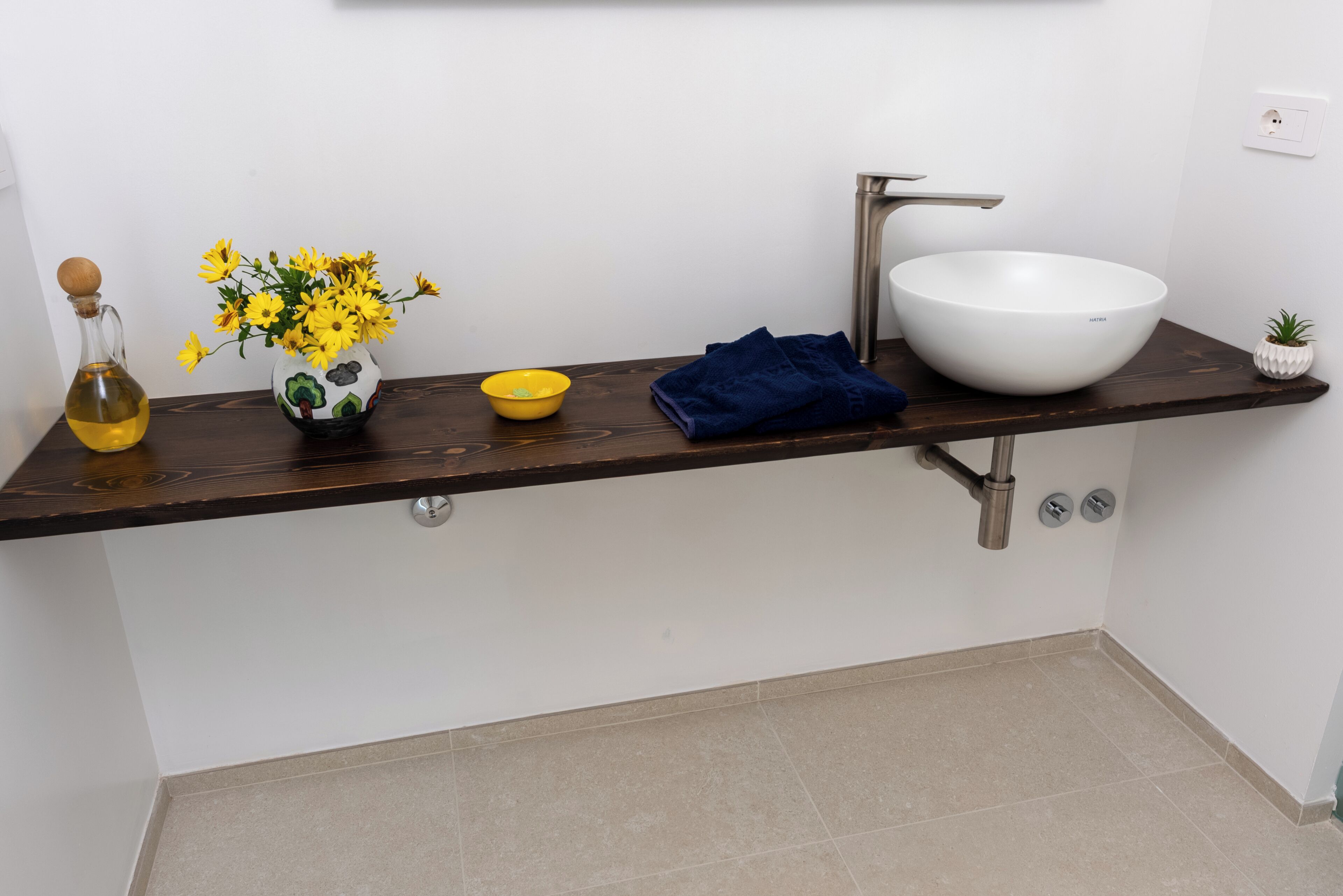 Ein modernes Badezimmer mit dunkler Holzplatte, einem weißen Waschbecken und einem kleinen Topfpflanzen.