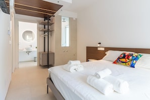 A modern hotel room with a neatly made bed, a colorful pillow, and a view of the bathroom.