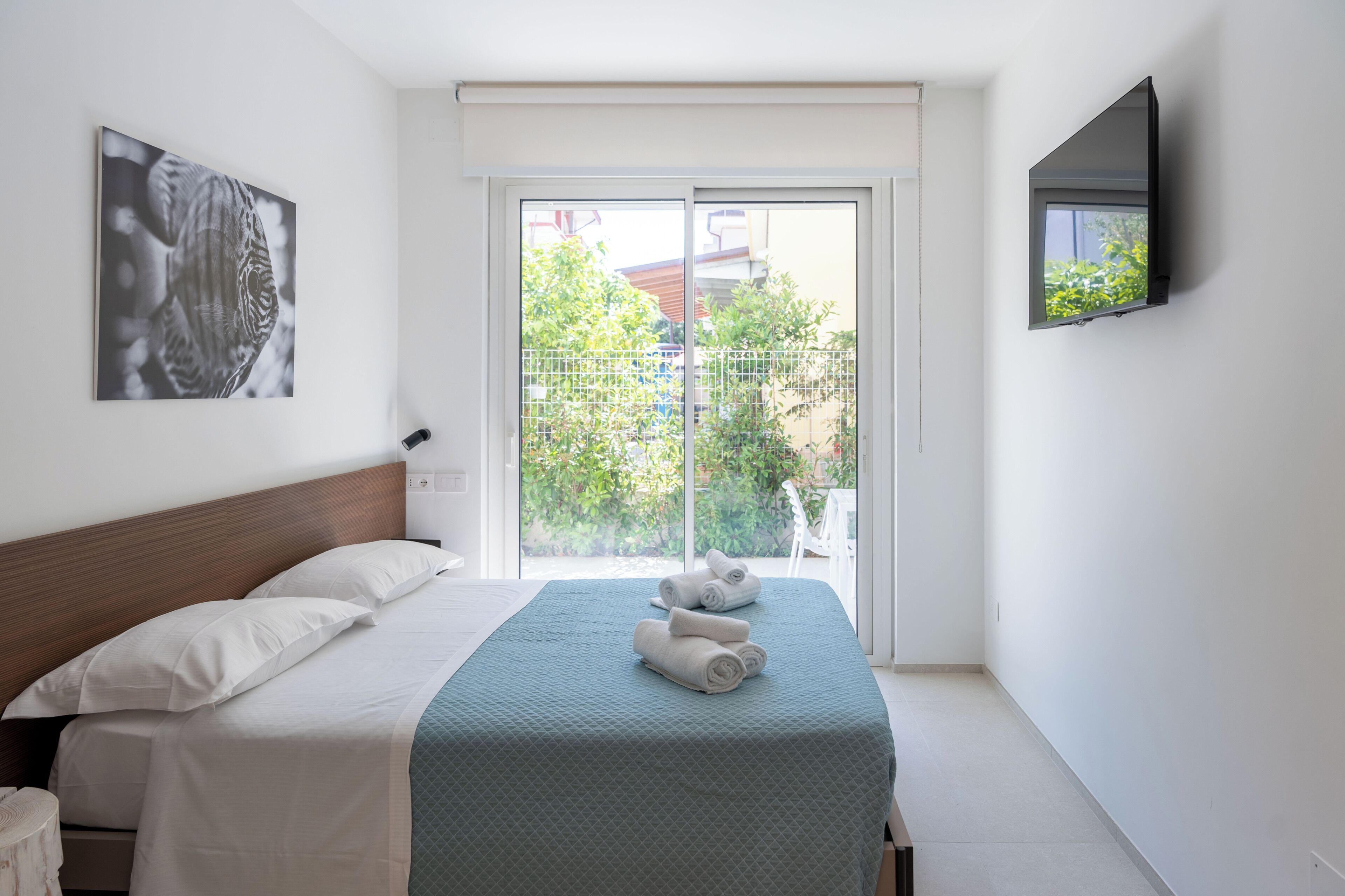 Een slaapkamer met een bed, een tv aan de muur en een raam met uitzicht op groen.