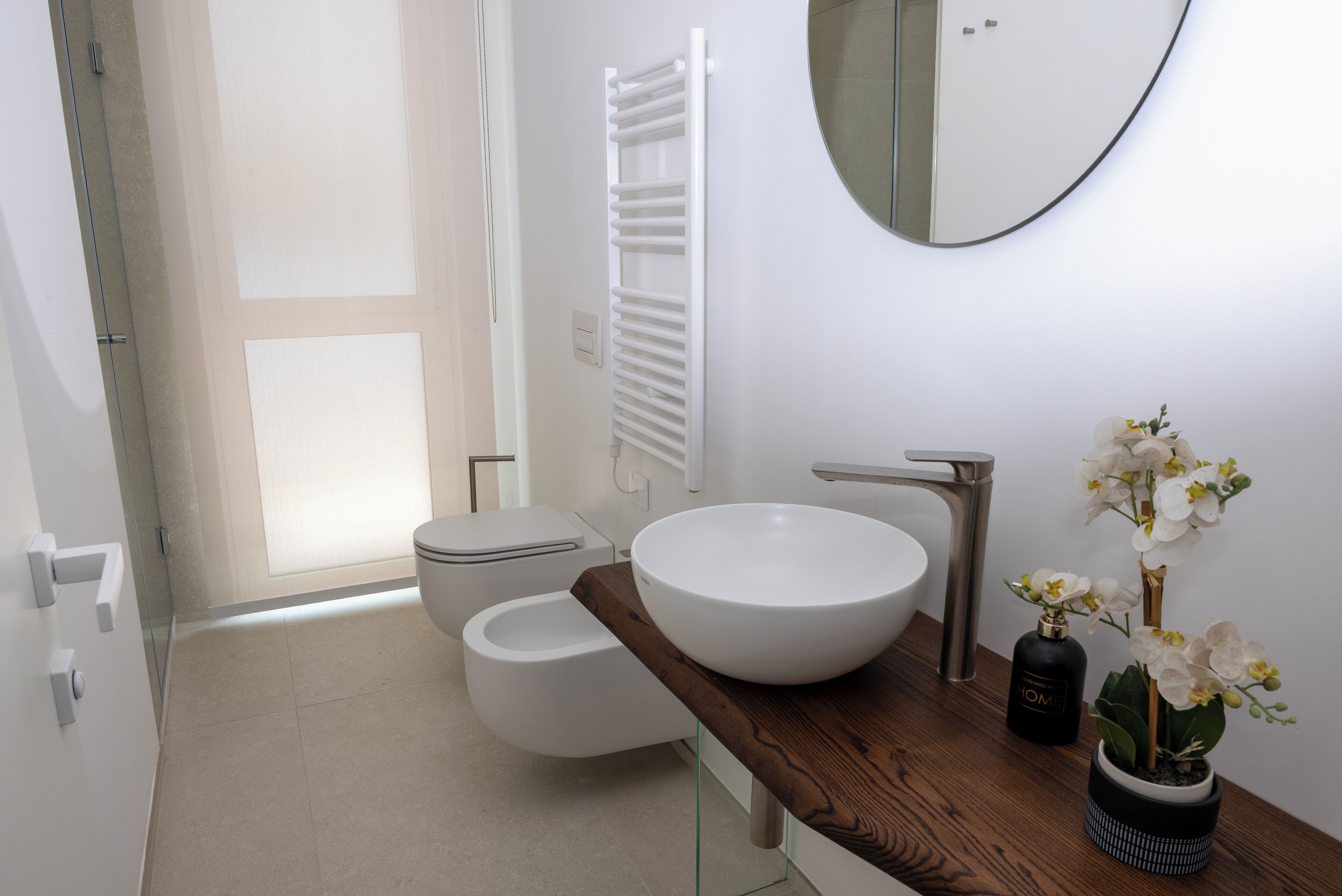 A modern bathroom with a large white sink, a toilet, a towel rack, and a mirror.