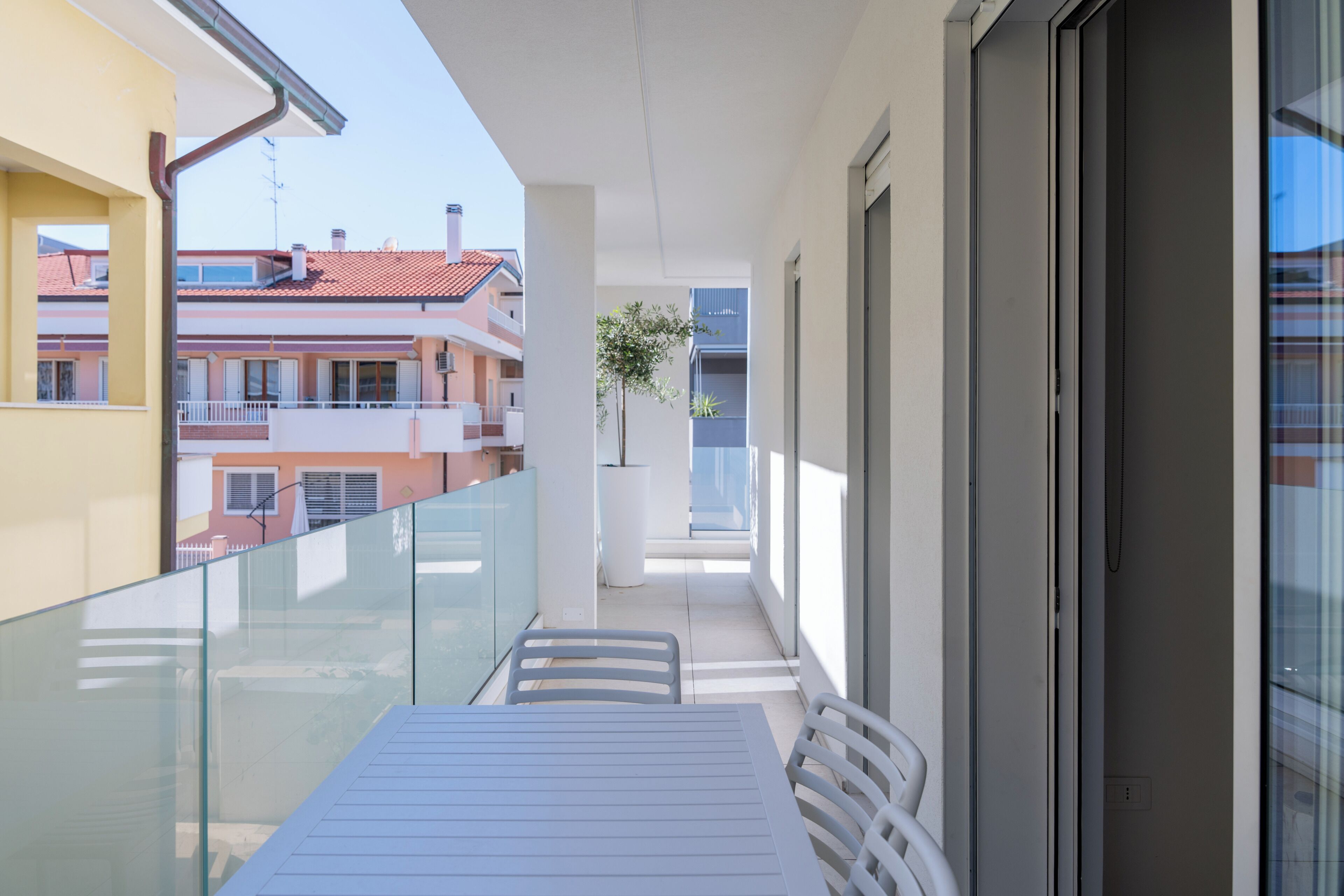 Un balcone con tavolo e sedie, una pianta in vaso e vista sugli edifici vicini.