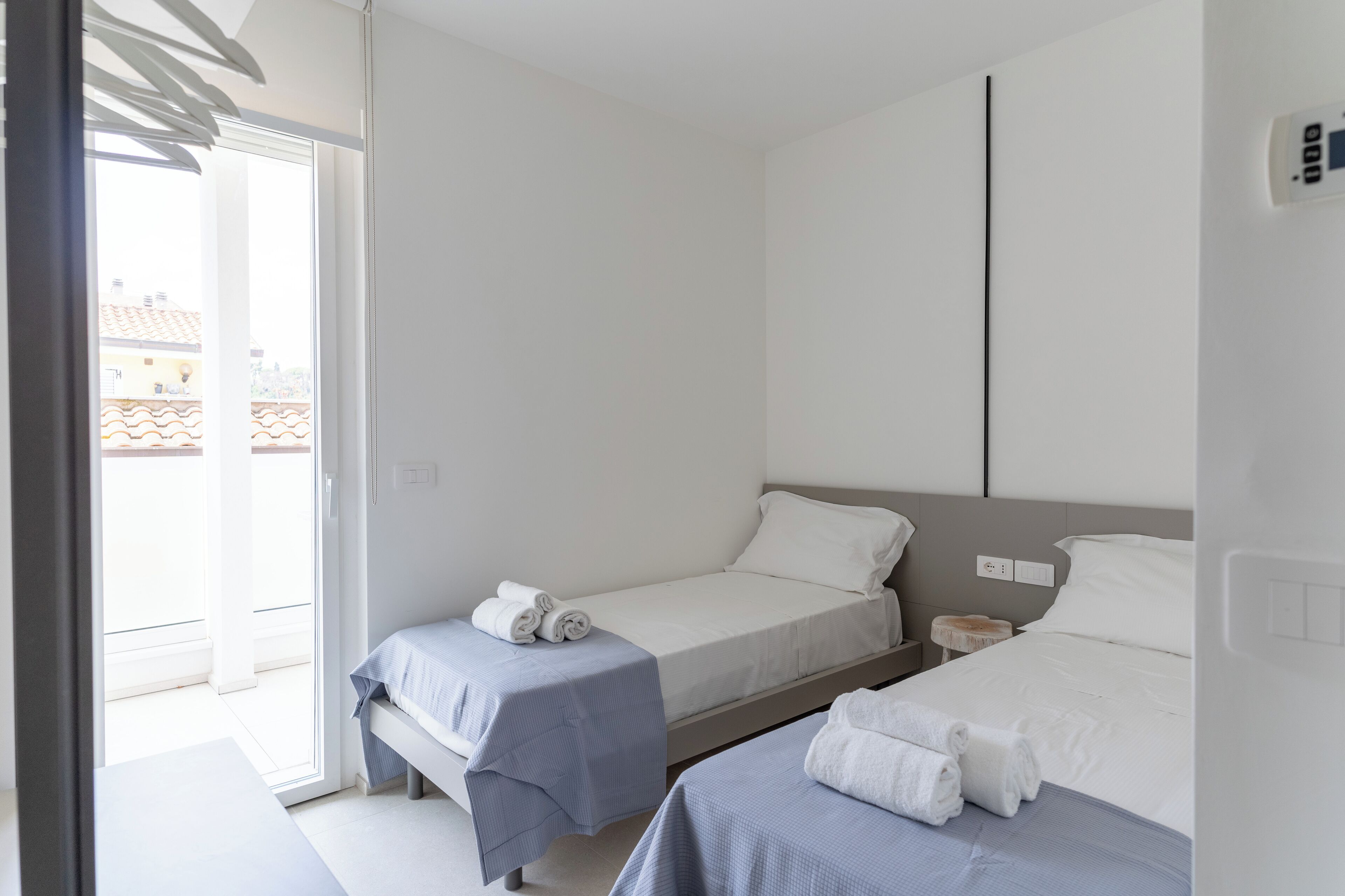 A hotel room with two beds, a small table, and a view of the outside.