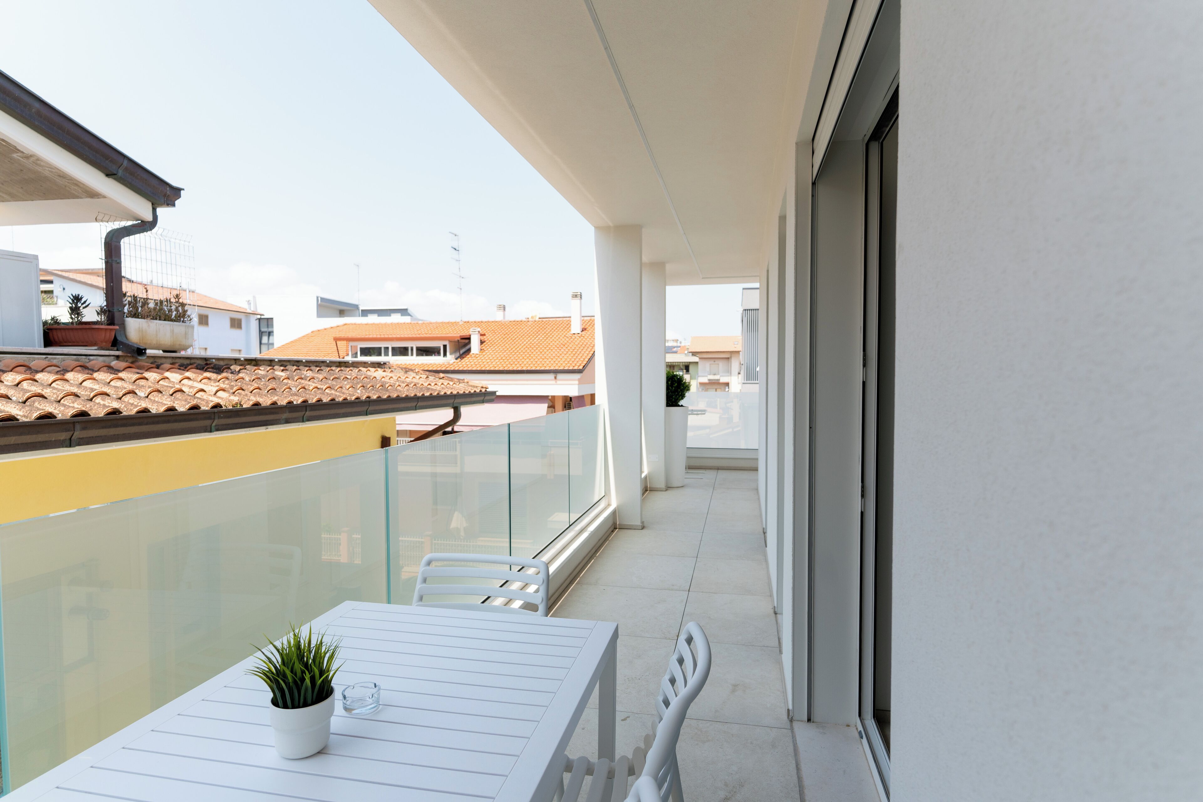 A balcony with a white table, chairs, and a potted plant.