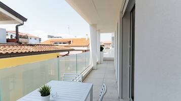 A balcony with a white table, chairs, and a potted plant.