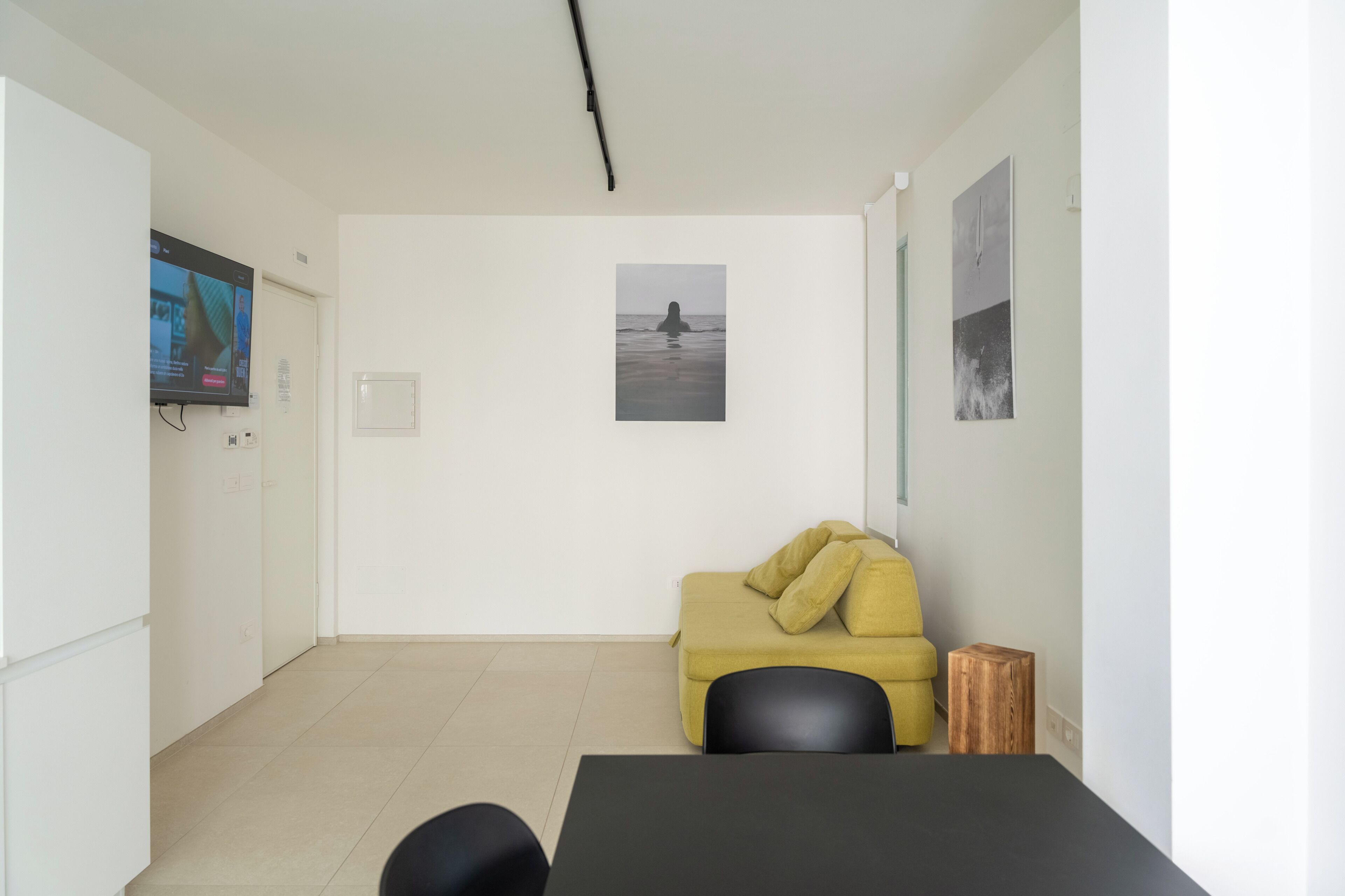 A modern, minimalistic room with a yellow sofa, a black table, and a television on the wall.