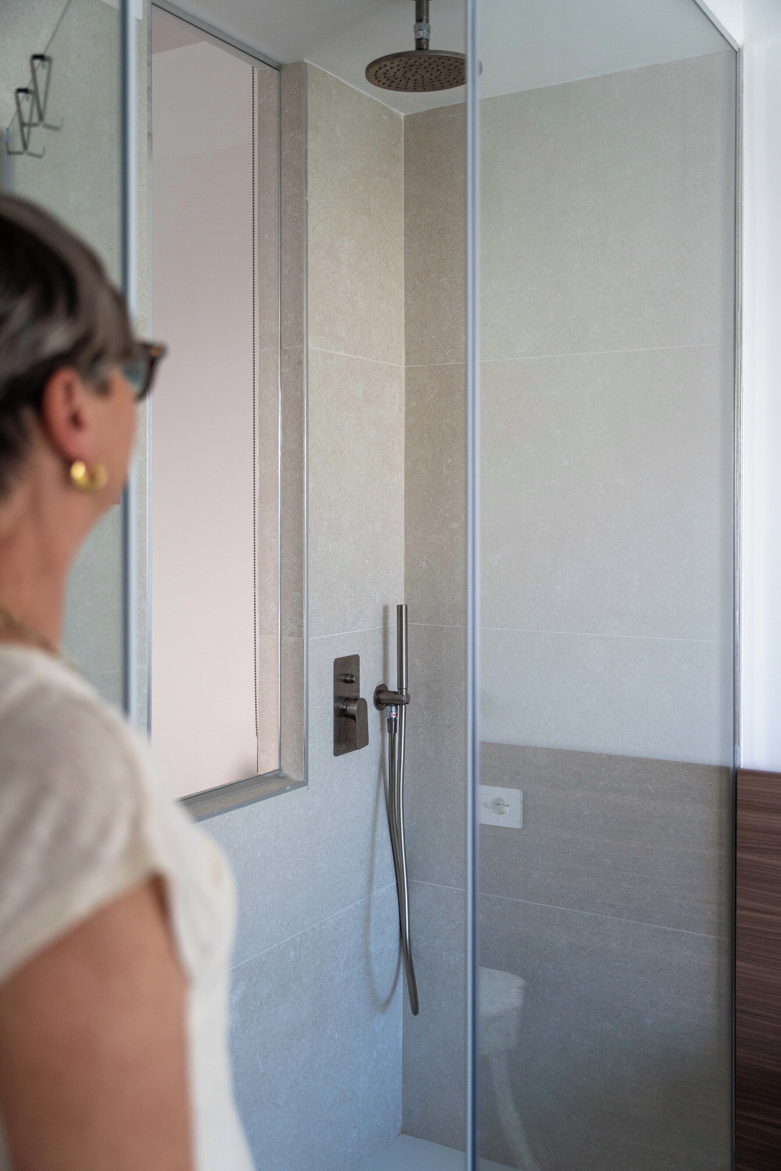 Une salle de bain moderne dotée d’une douche à parois de verre, d’un panneau de commande visible et d’une porte donnant sur une autre pièce.