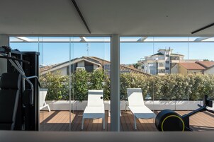 Una palestra con attrezzature per esercizi, un tavolo e sedie su un pontile di legno con vista su edifici e alberi.
