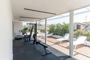 Una palestra moderna con attrezzature per esercizi e vista su un patio con poltrone bianche da relax.