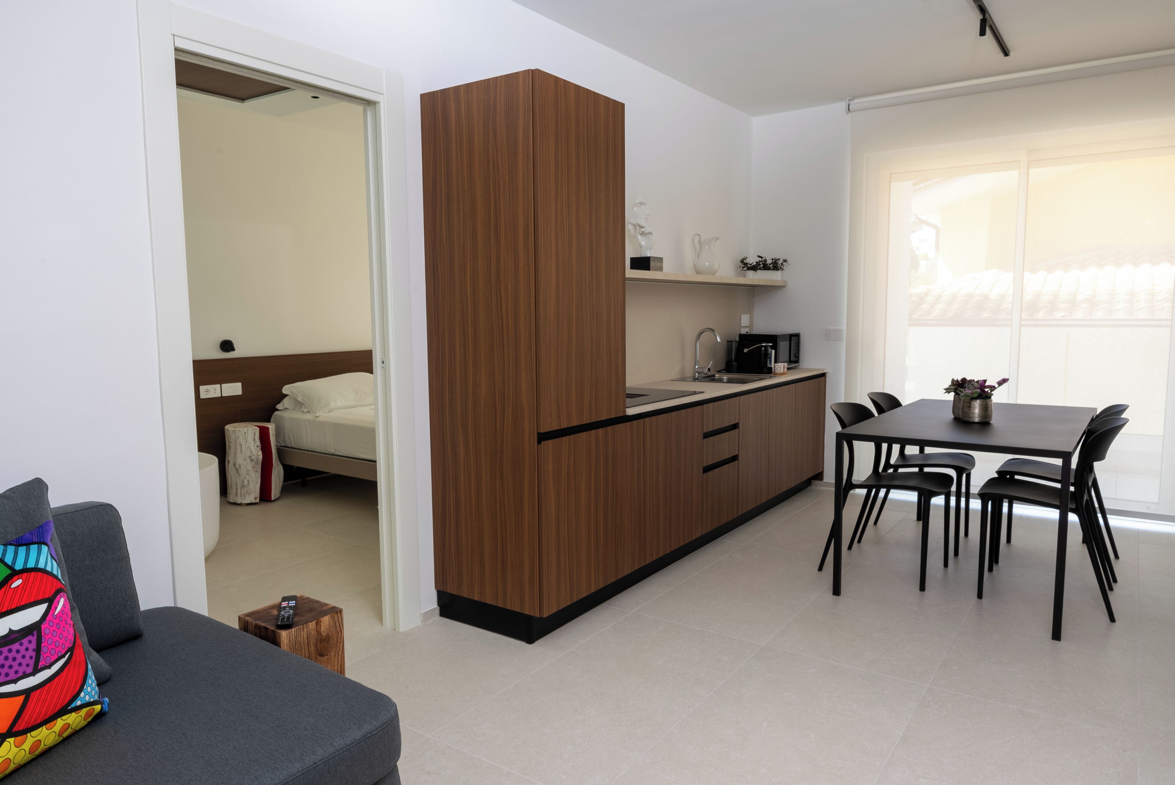 A compact living space with a kitchenette, dining area, and a bed in the adjacent room.