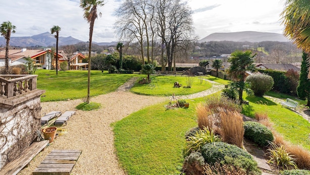 Ein angelegter Garten mit einer Holzbank, einem Steinweg und Blick auf Häuser und Berge im Hintergrund.